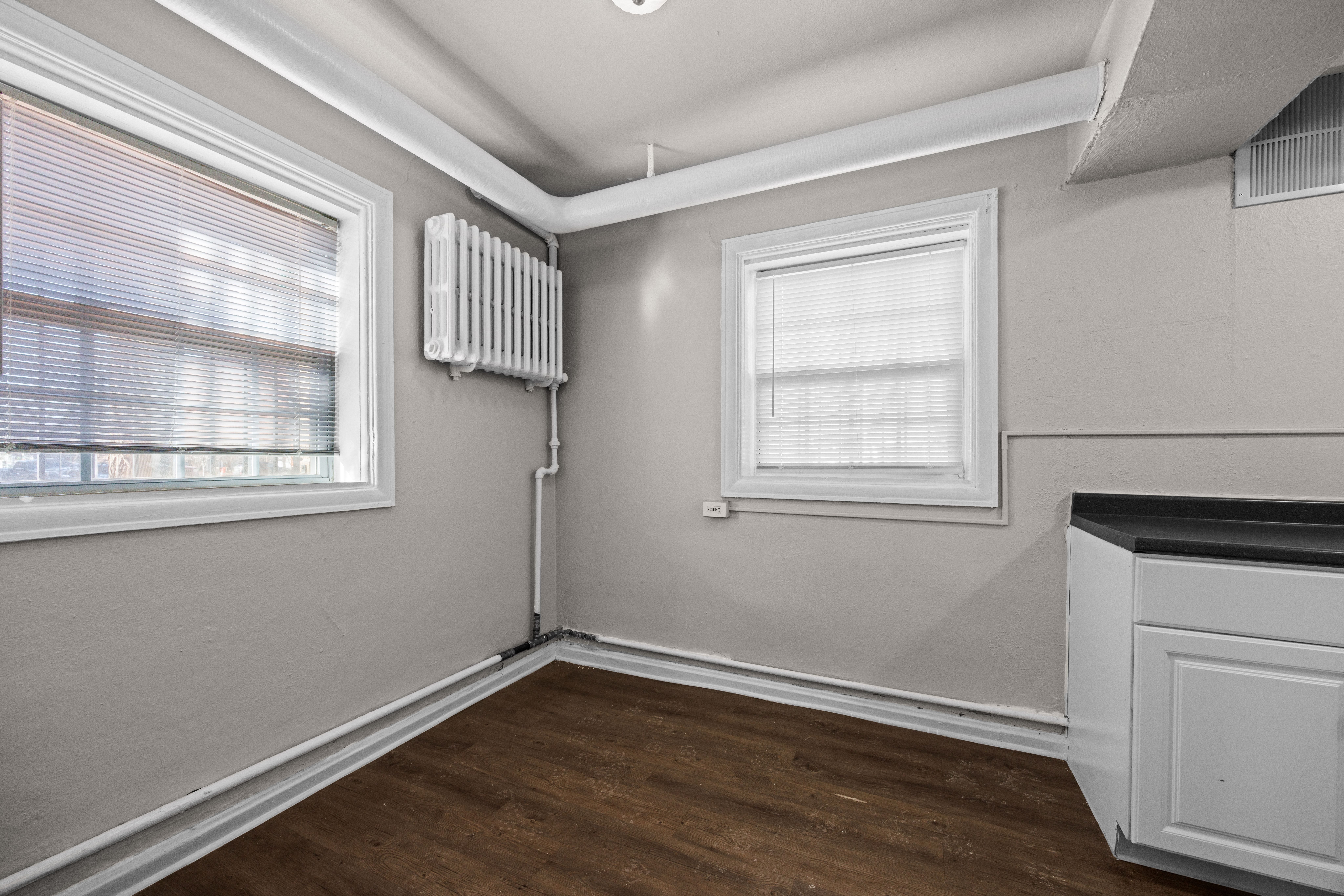 A room with a window, a radiator, and a wooden floor.